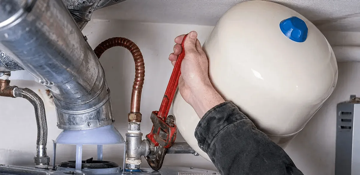 Water heater repair technician tightening plumbing connections near a tank unit in Tempe, AZ
